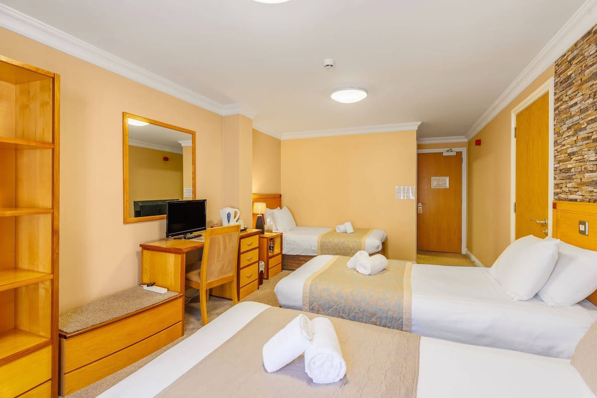A hotel room with two beds, a desk with a computer, a chair, and a wardrobe.
