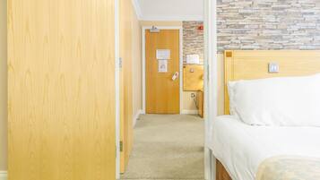 Habitación de hotel con un armario de madera, una cama con colcha estampada, una pared de piedra y suelo alfombrado.