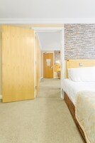 Habitación de hotel con un armario de madera, una cama con colcha estampada, una pared de piedra y suelo alfombrado.