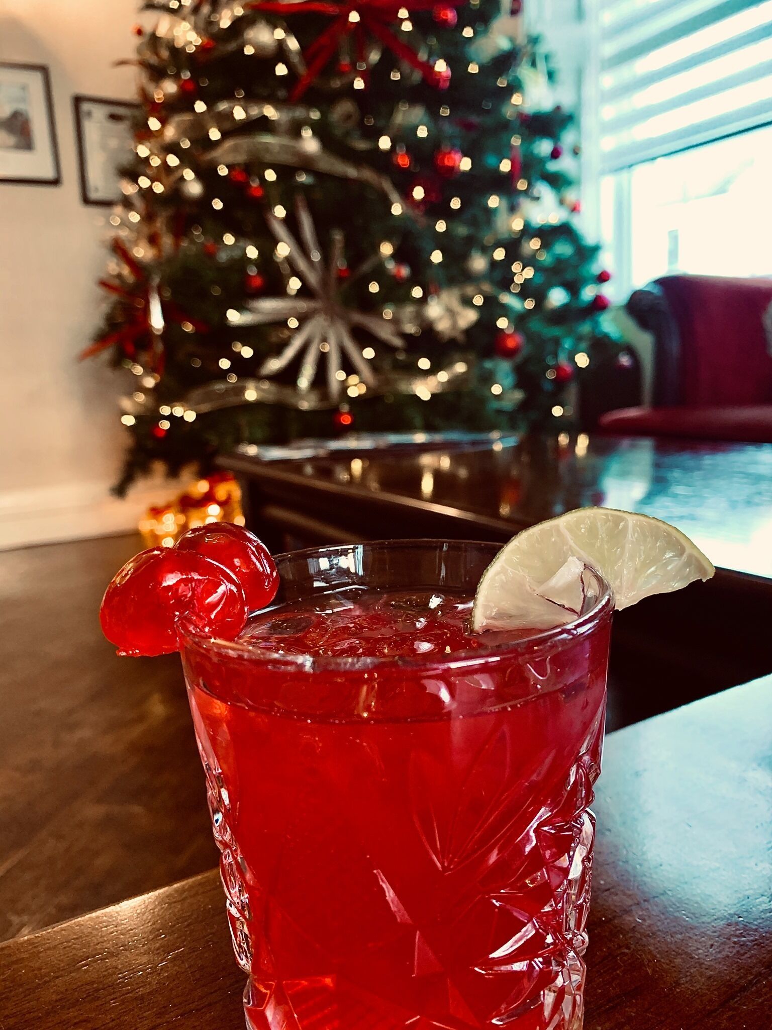Een glas met een rood drankje, versierd met een partje citroen en een kers, op een houten tafel.