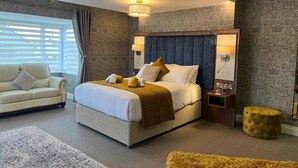 A bedroom with a large bed, a sofa, a nightstand, and a small ottoman. - Kilmorey Arms Hotel (Newry)