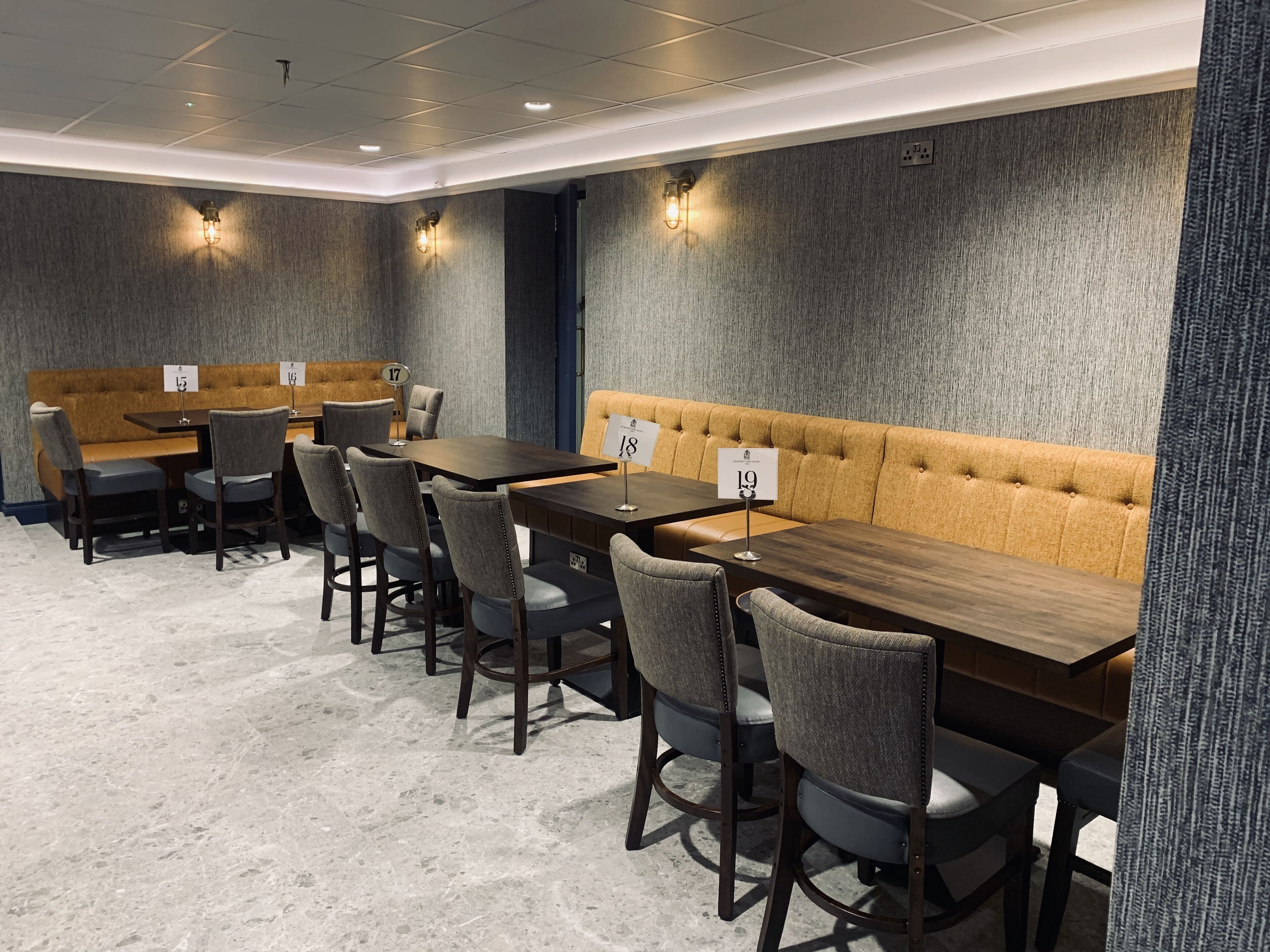 A modern dining area with a long wooden table, grey upholstered chairs, and a yellow cushioned bench.