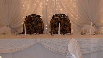 Una mesa de banquete dispuesta con manteles blancos, sillas elegantes y candelabros.