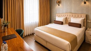 Une chambre d’hôtel avec un grand lit, un bureau en bois, une chaise, une table de chevet avec une lampe et une fenêtre avec des rideaux.