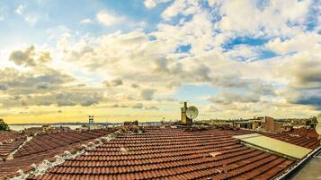 Una azotea con tejas rojas, antenas parabólicas y vistas de un paisaje urbano bajo un cielo parcialmente nublado.