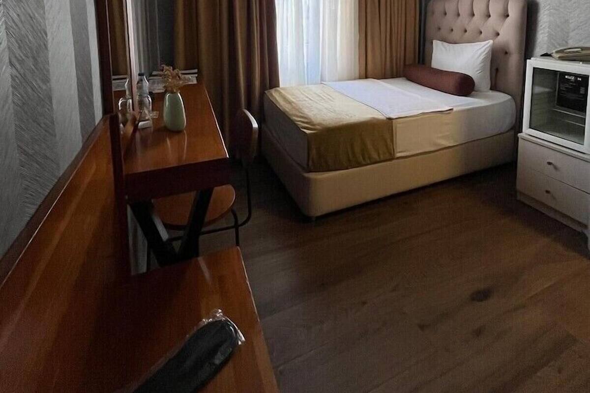 A hotel room with a bed, a desk, a chair, a television, and a window with curtains.