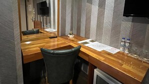 Une chambre d’hôtel compacte comprenant un bureau en bois, une chaise, un téléviseur à écran plat fixé au mur et un mini-bar.