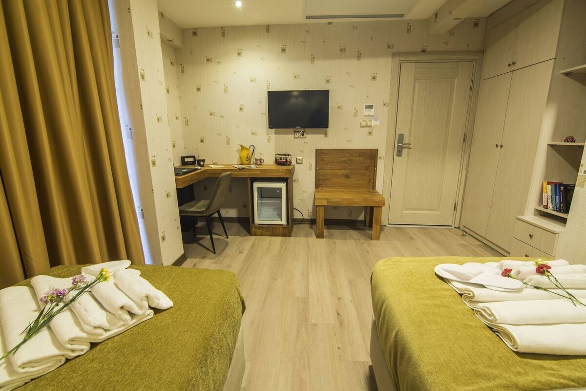 A hotel room with two beds, a desk, a chair, a television, and a wardrobe.