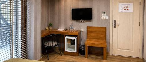 A compact room with a wooden desk, a television, a door with a notice, and a small refrigerator.