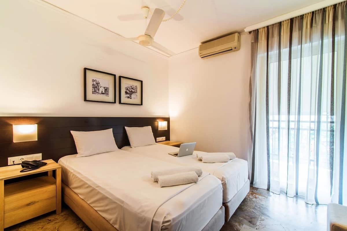 Una habitación de hotel con dos camas, un escritorio con una computadora portátil, un teléfono y cuadros en la pared.