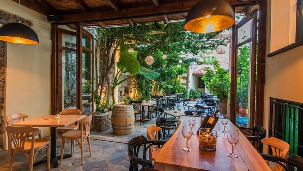 Un espace de restauration en plein air doté d’un sol en pierre, de tables et de chaises en bois, et de luminaires suspendus.