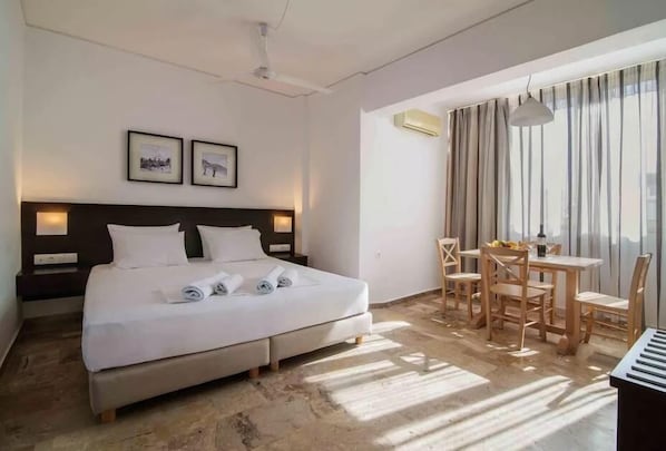 A hotel room with a bed, a desk, and a chair. There are two framed pictures on the wall.