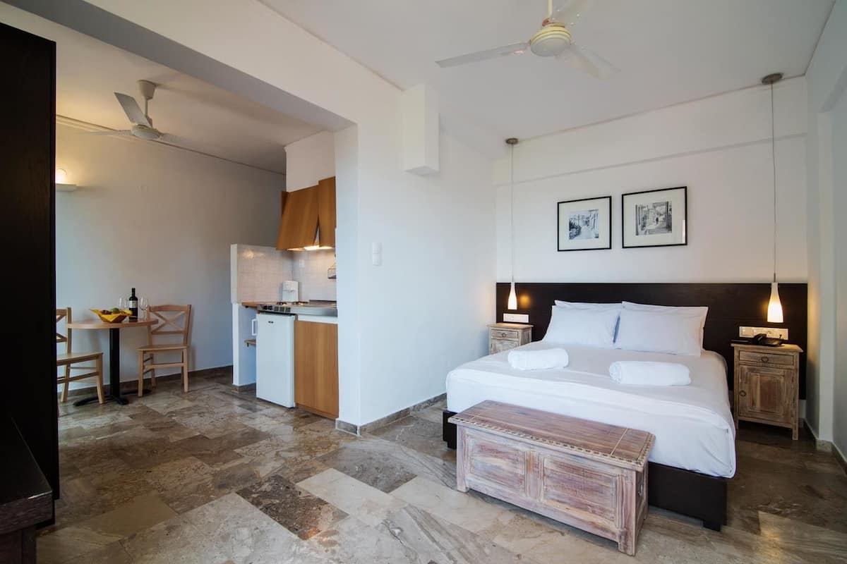 Habitación de hotel con cama, mesitas de noche, escritorio con silla, kitchenette y comedor.