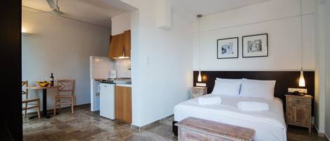 A hotel room with a bed, bedside tables, a desk with a chair, a kitchenette, and a dining area.
