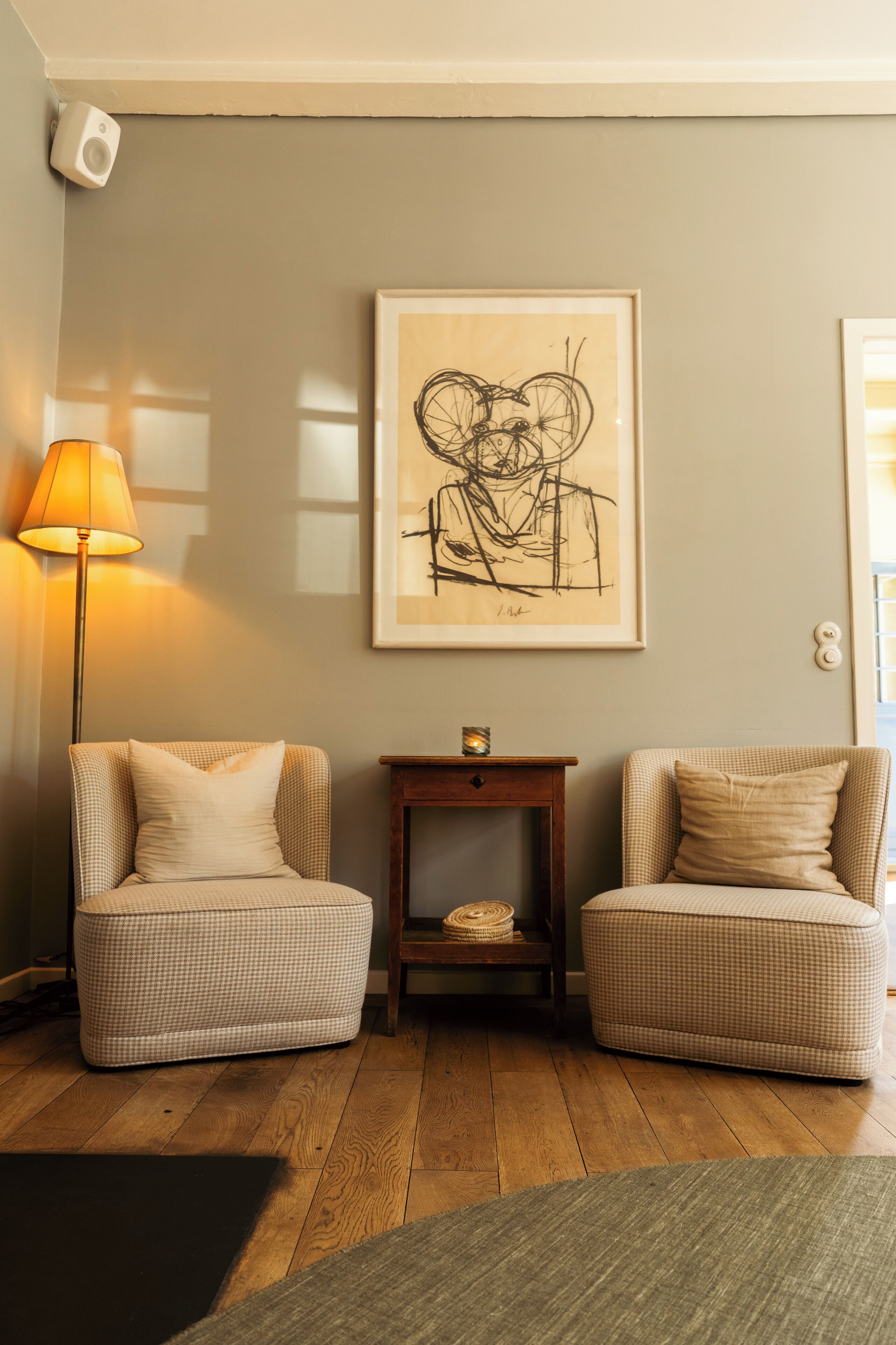 Une pièce comprenant deux fauteuils à motifs à carreaux, une petite table d’appoint en bois et une œuvre d’art abstraite encadrée accrochée au mur.