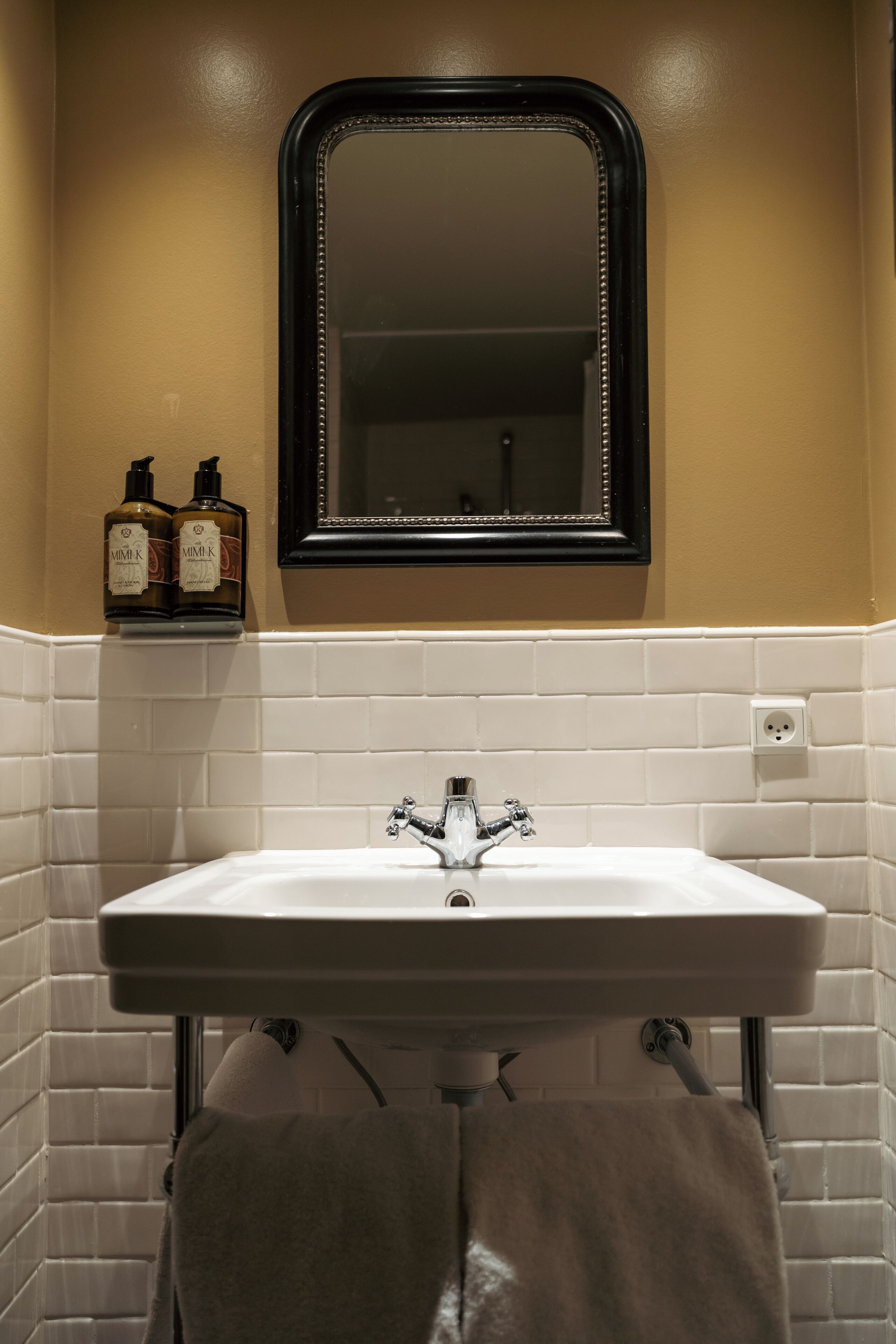 Baño con lavamanos blanco, un espejo y dos botellas de champú en un estante.