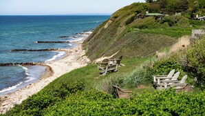 A coastal landscape with a beach, wooden chairs, and a house on a hill. - Helenekilde Badehotel (Tisvildeleje)
