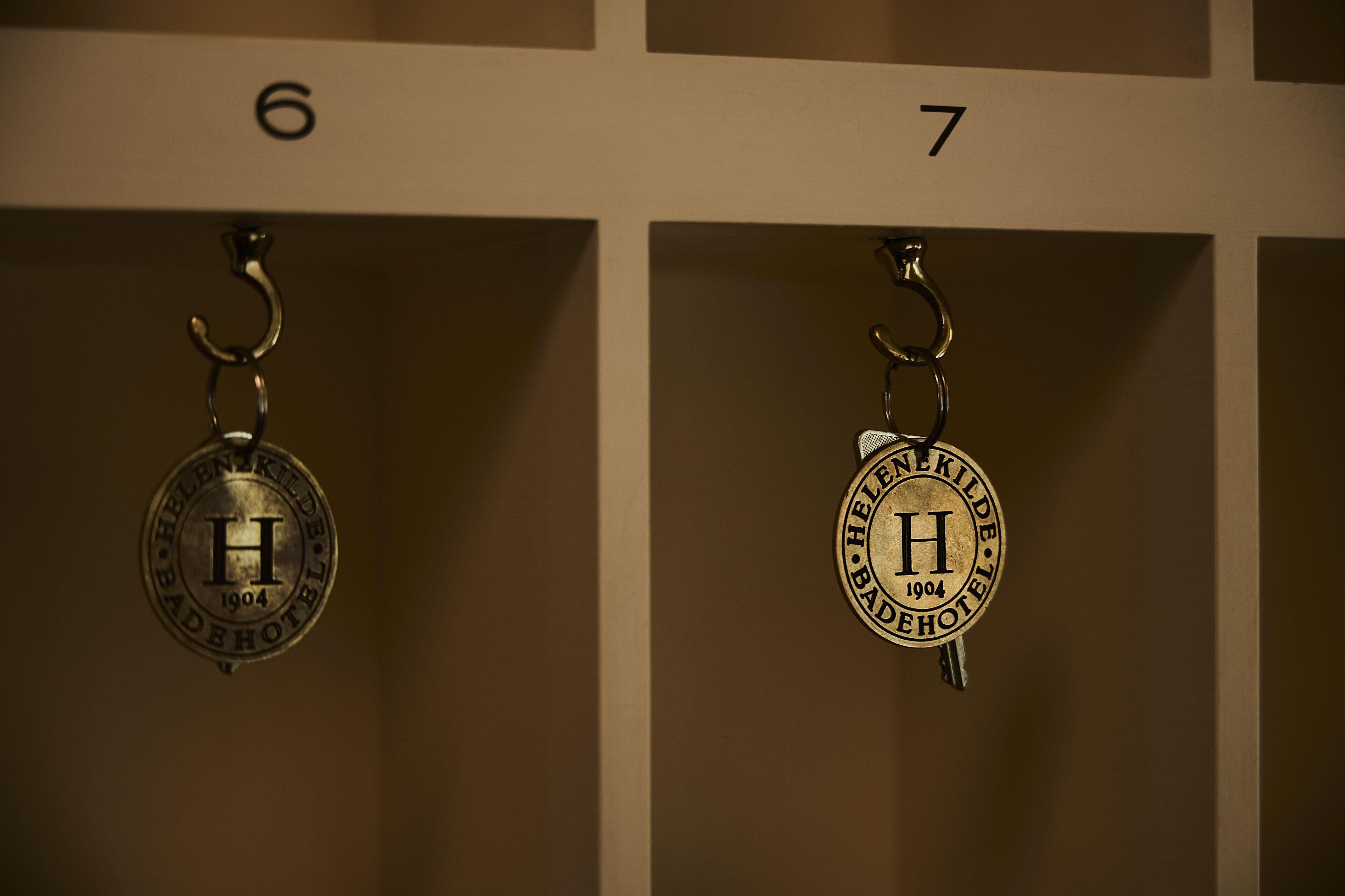 Two keychains with the emblem of the Helene Kilde hotel from 1904.