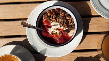 Ein Frühstücksbuffet mit Joghurt, Granola und Beeren, einem Glas Orangensaft, Käse und Trauben, Brotscheiben und einer Kaffeetasse mit Latte Art.