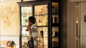 A person walking through a room with a wooden floor, a glass cabinet with bottles, and a wall with a map. - Helenekilde Badehotel (Tisvildeleje)