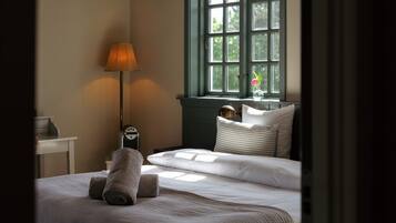 Una cama bien hecha con una almohada, una lámpara de noche y una ventana con vistas a la vegetación.