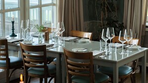 A dining table set for six with a view of the sea through large windows. - Helenekilde Badehotel (Tisvildeleje)