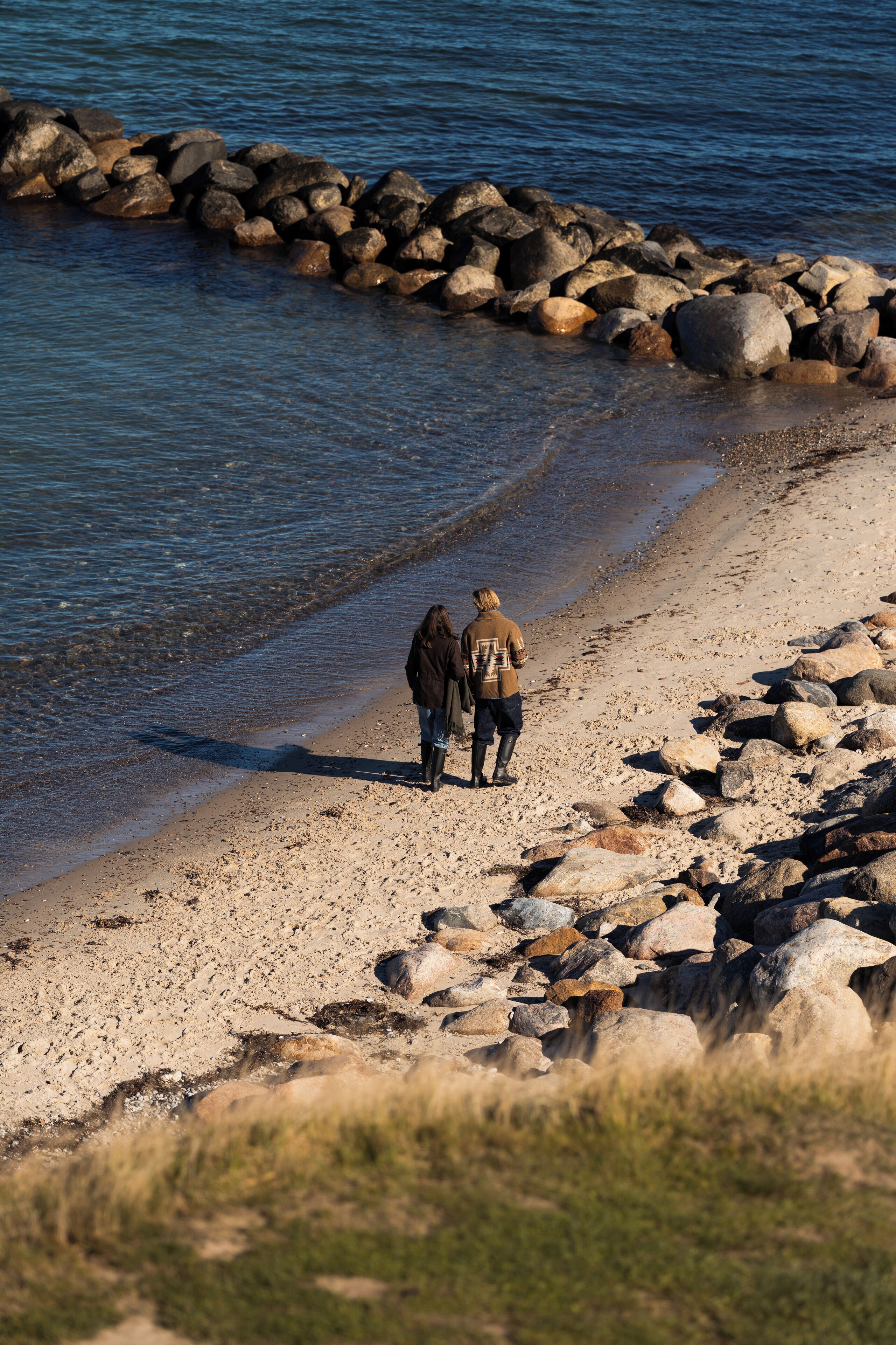 Una playa rocosa con dos personas caminando por la orilla.