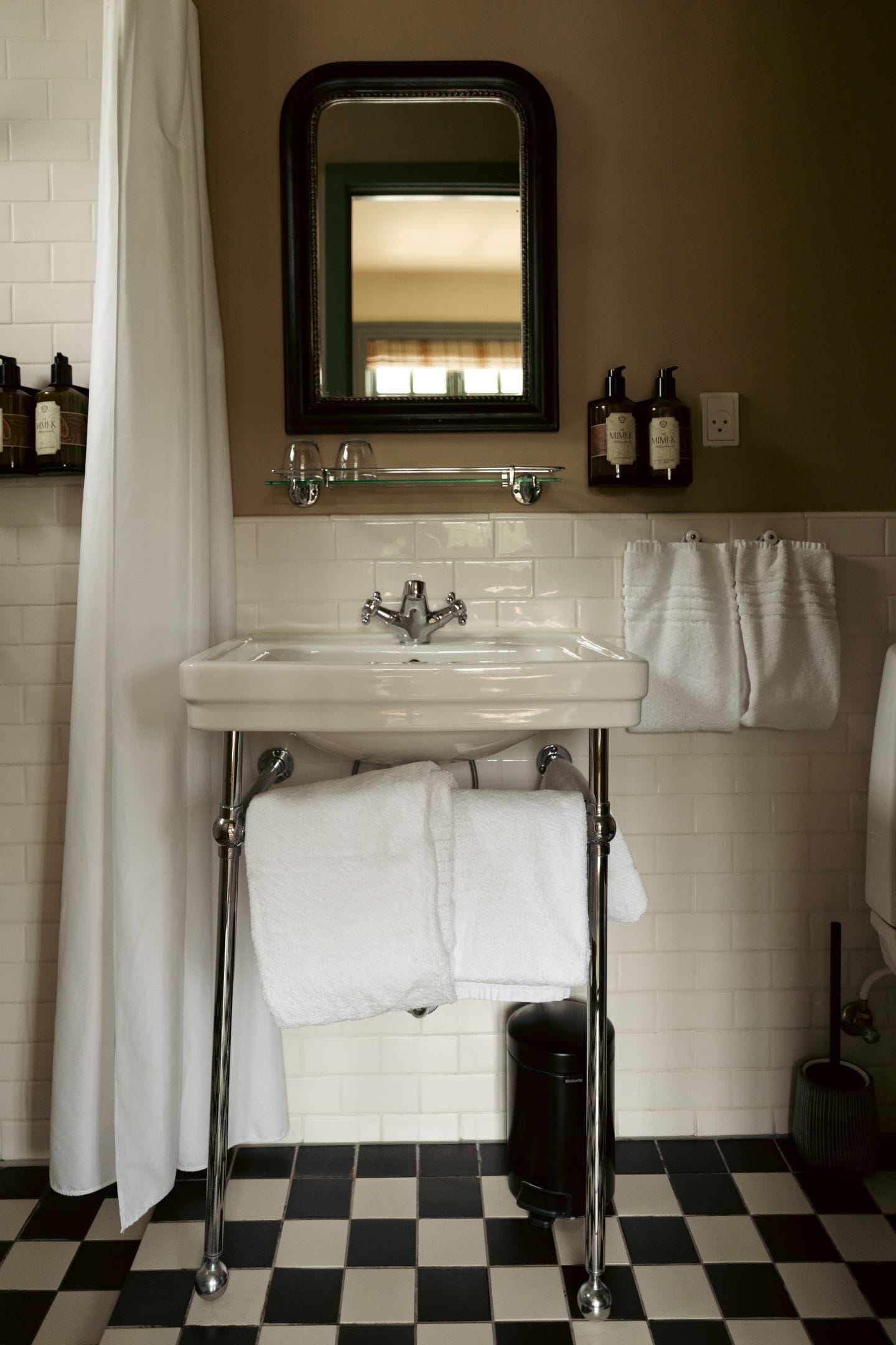 Un baño con un lavabo blanco, un espejo y un cubo de basura negro.