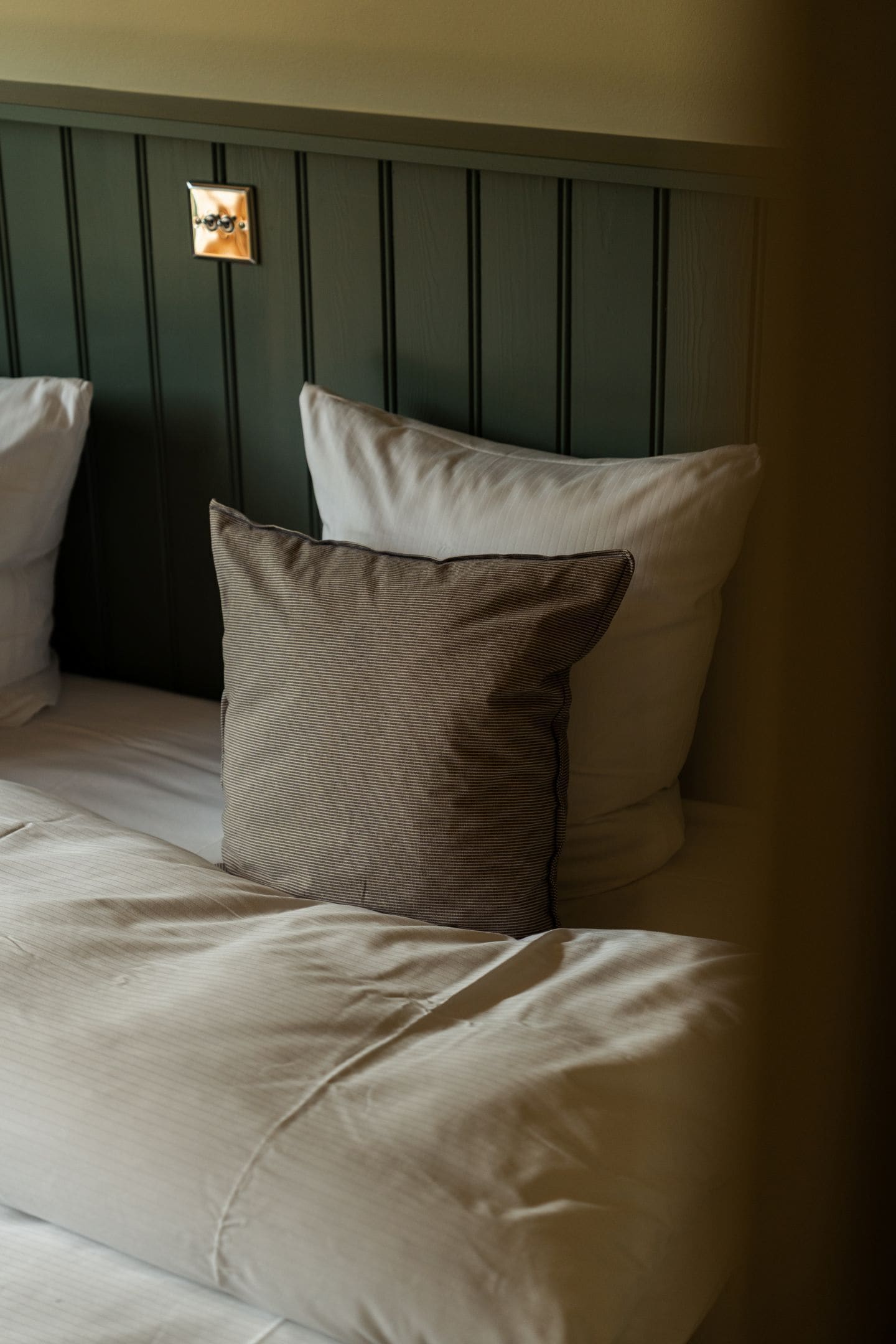 A bed with two pillows, a headboard, and a wall-mounted light fixture.