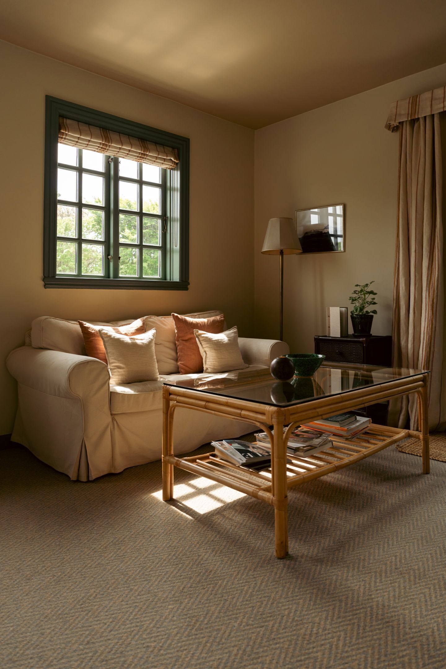 A living room with a sofa, a glass coffee table, a lamp, a potted plant, and a window with curtains.