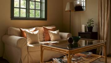 A living room with a sofa, a glass coffee table, a lamp, a potted plant, and a window with curtains.