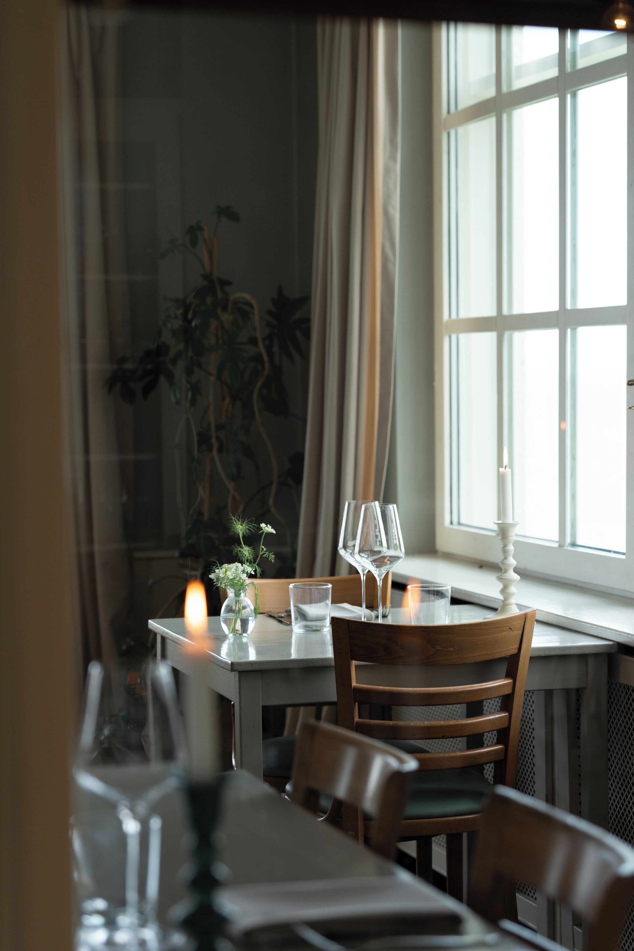 Una mesa de comedor con sillas, una vela y una ventana con cortinas.