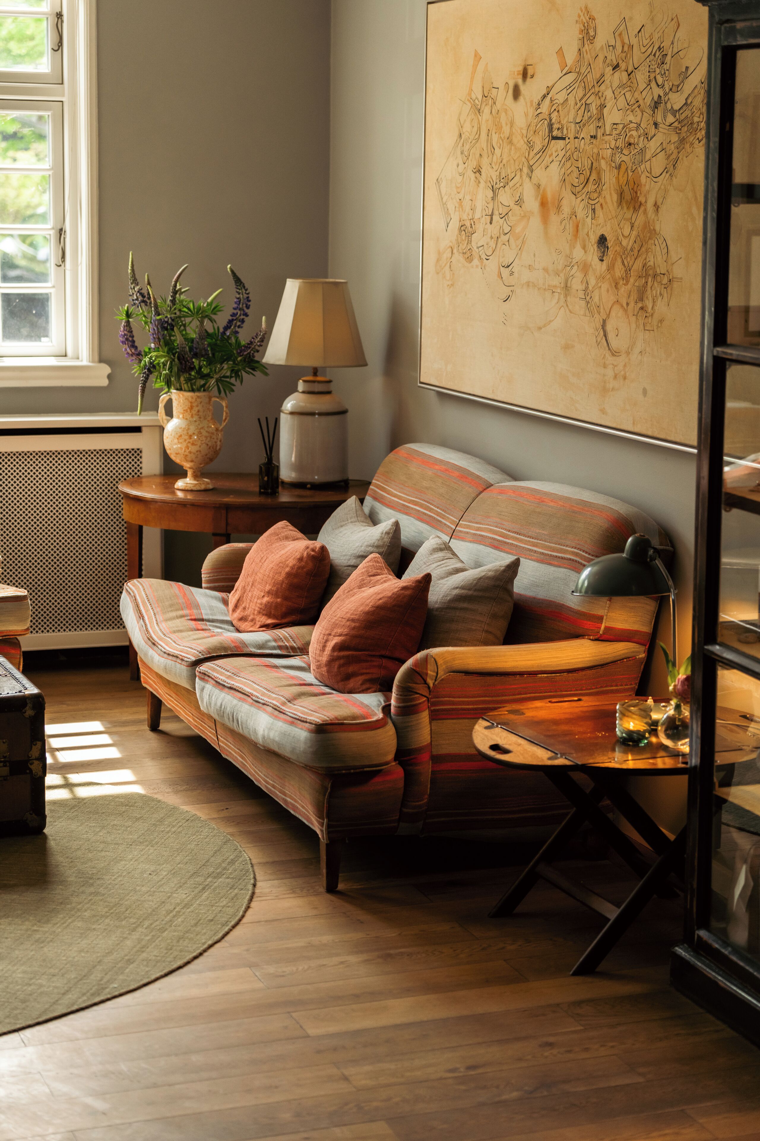 A cozy living room with a sofa, a lamp, and a large abstract painting on the wall.