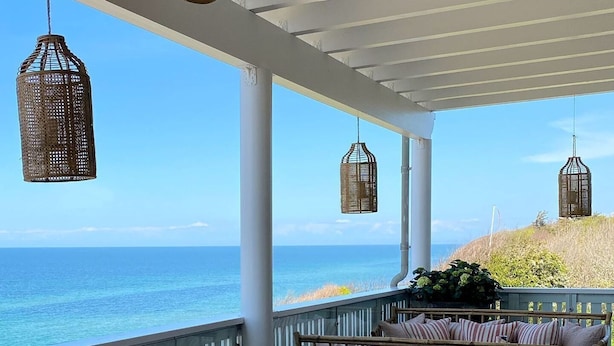 A covered outdoor seating area with wicker furniture and cushions, overlooking a beach. - Helenekilde Badehotel (Tisvildeleje)