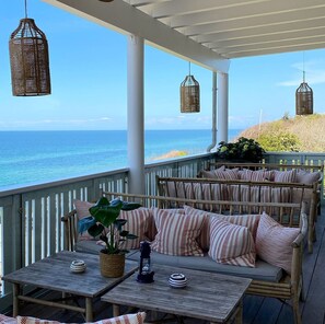 A covered outdoor seating area with wicker furniture and cushions, overlooking a beach. - Helenekilde Badehotel (Tisvildeleje)