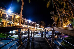 A hotel entrance with a pool area, outdoor seating, and palm trees.