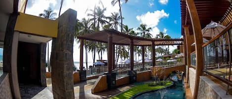 A pool area with a small water feature, surrounded by palm trees and a covered seating area.