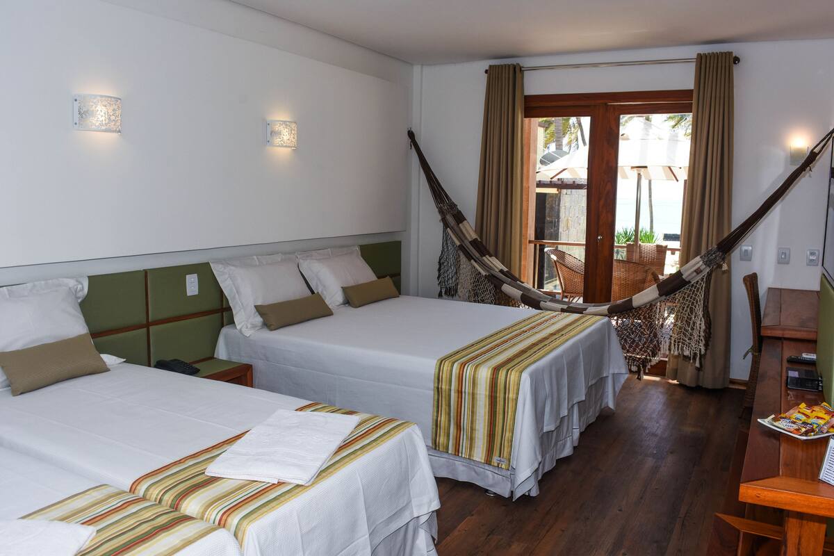 A hotel room with two beds, a hammock, a wooden desk, and a view of the outdoors.