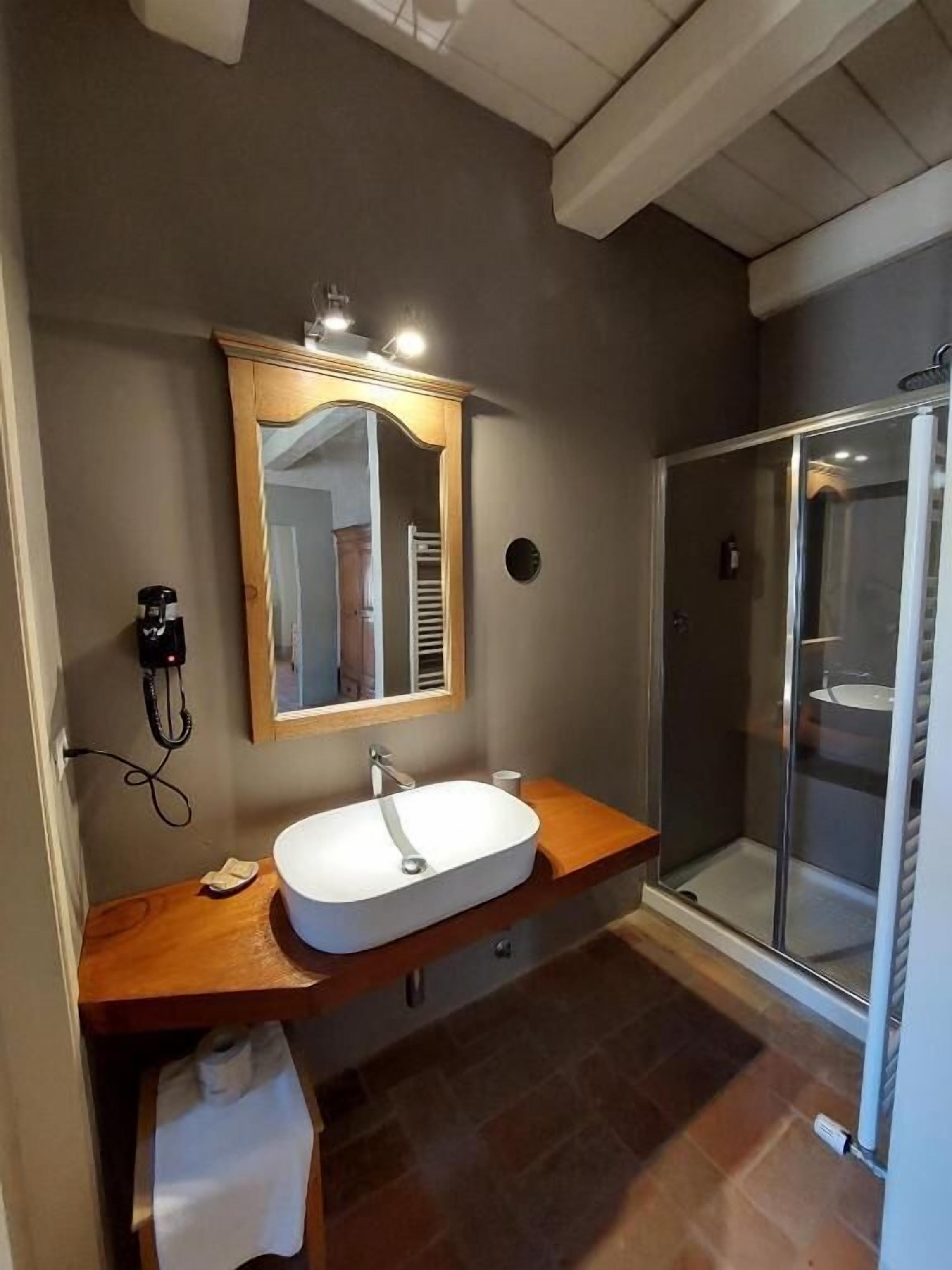 A bathroom with a wooden vanity, a white sink, a mirror, and a glass-enclosed shower.