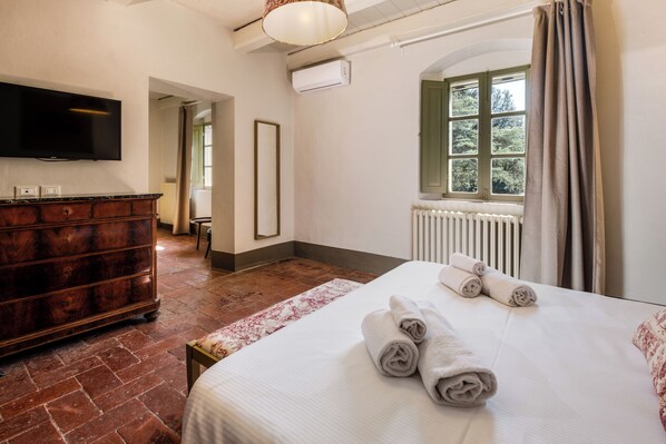 Una habitación de hotel con cama, cómoda, televisor, ventana con cortinas y radiador.