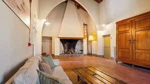 A cozy living area with a fireplace, a sofa, a wooden table, and a large wooden cabinet. - Tenuta la Fratta (Sinalunga)