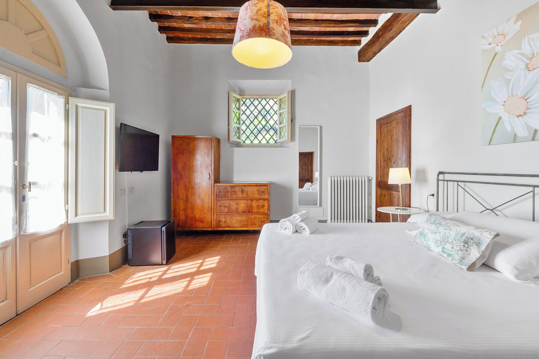 A bedroom with a bed, a wooden wardrobe, a radiator, a TV, and a window with a view.