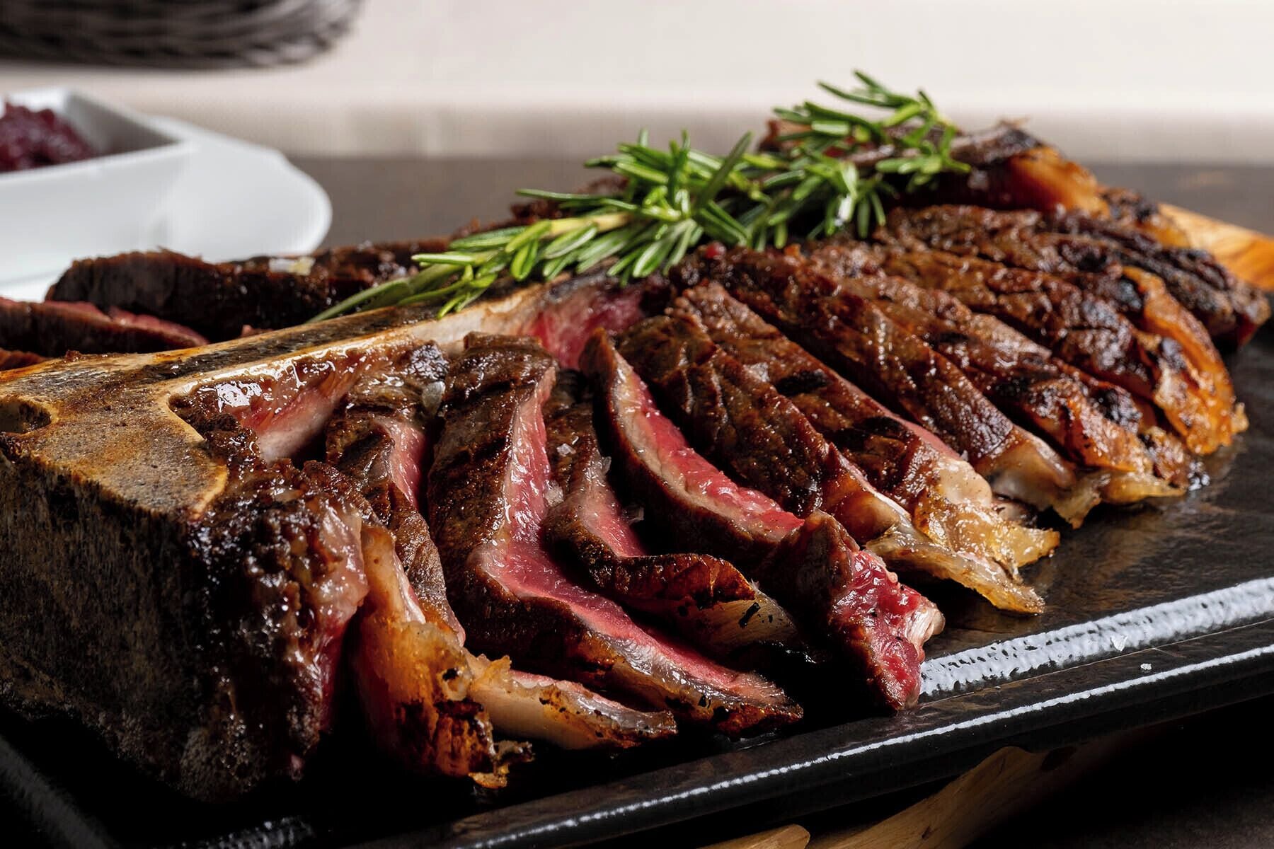 Ein Steak mit Rosmarinzierde auf einem schwarzen Teller.