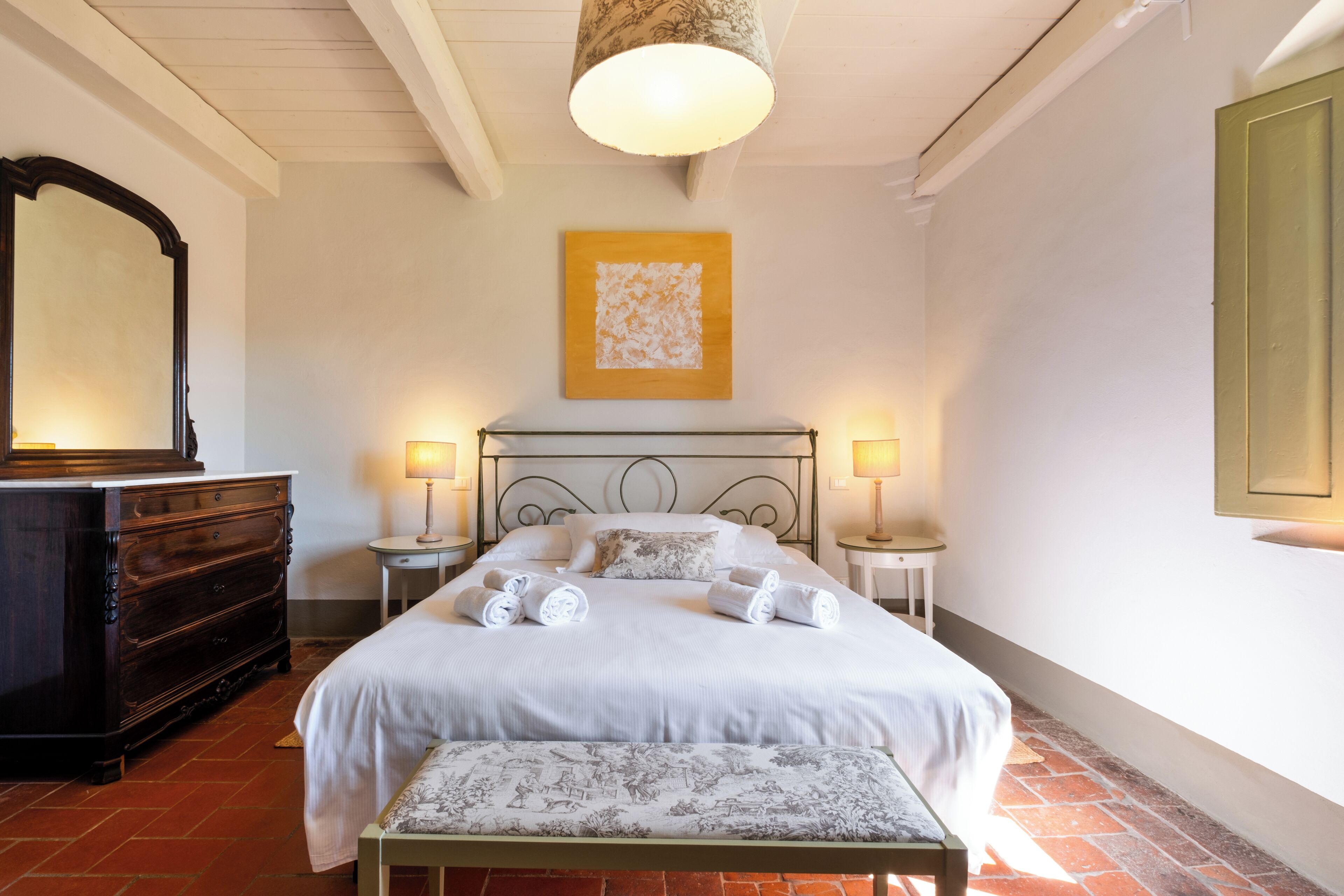 A bedroom with a bed, bedside tables, a dresser, a hanging light fixture, and a wall-mounted artwork.