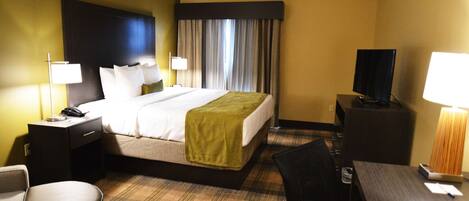 A hotel room with a bed, a desk, a chair, a television, and a lamp.
