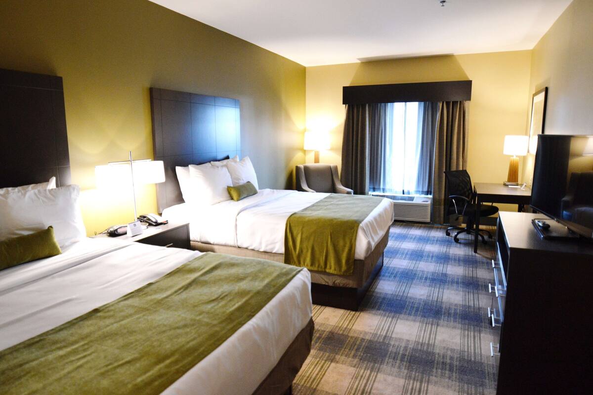 A hotel room with two beds, a desk, a chair, and a television.