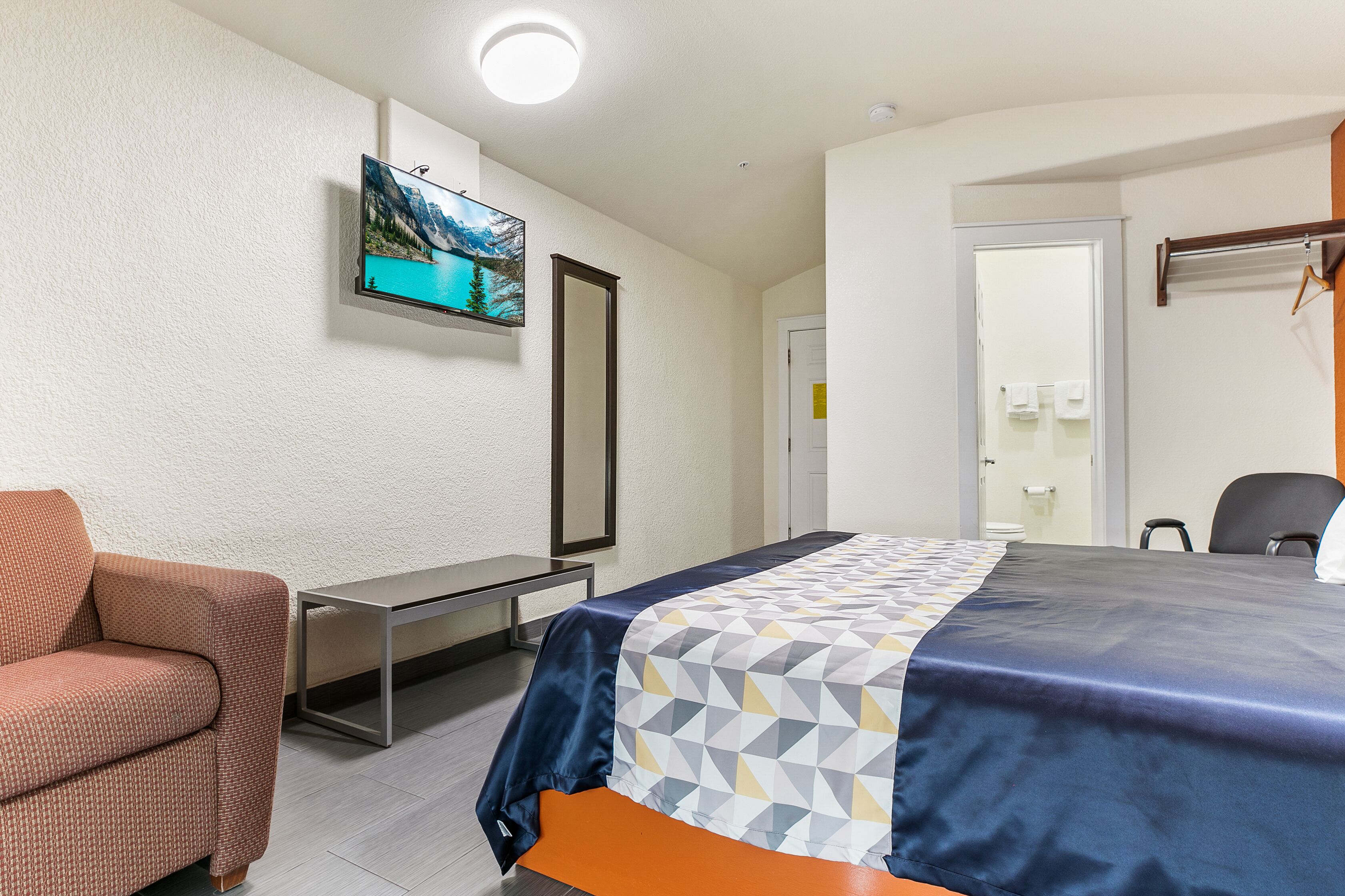 Una habitación de hotel con cama, televisión montada en la pared, escritorio y silla.