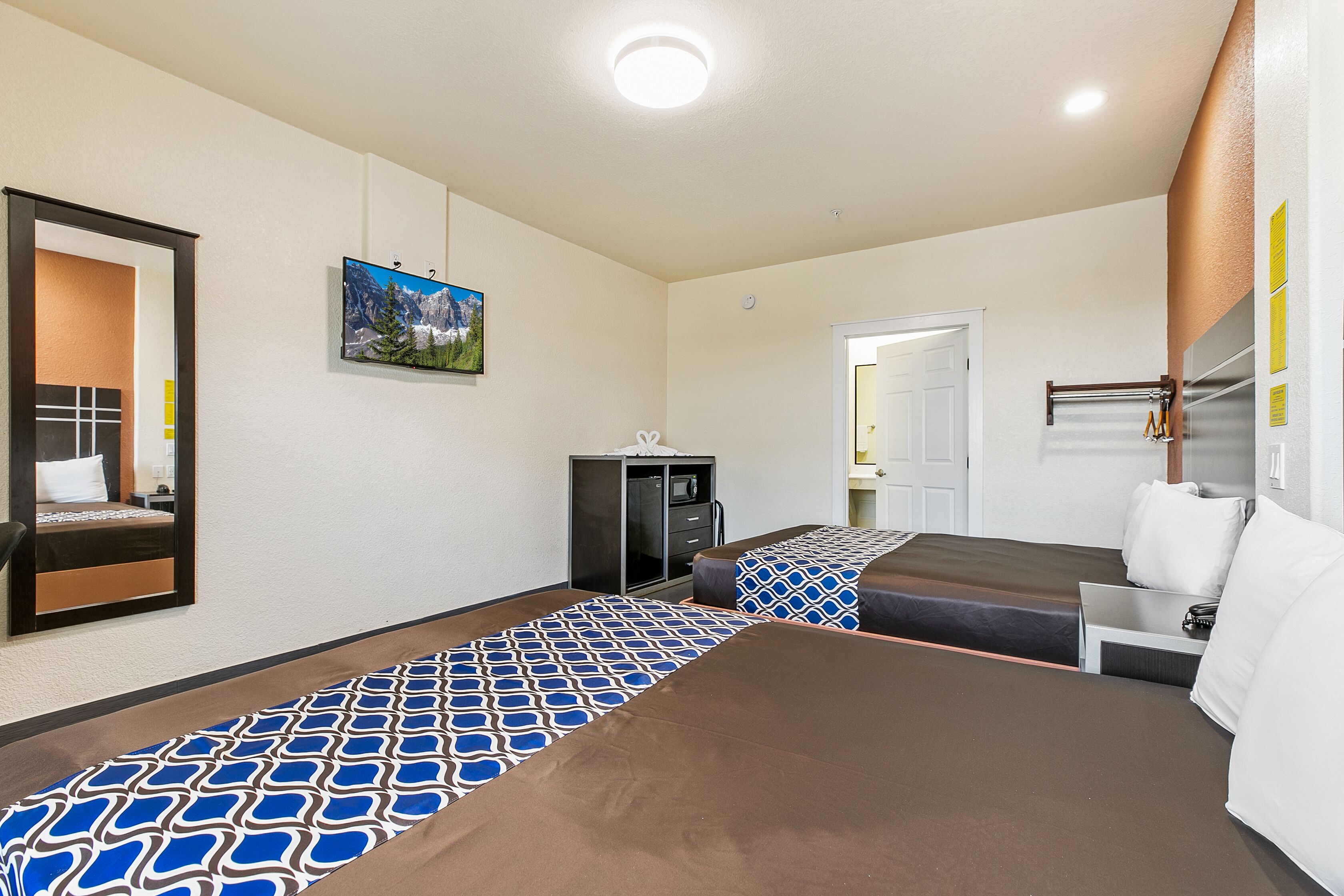 Une chambre d’hôtel avec deux lits, un bureau, une armoire et un téléviseur.
