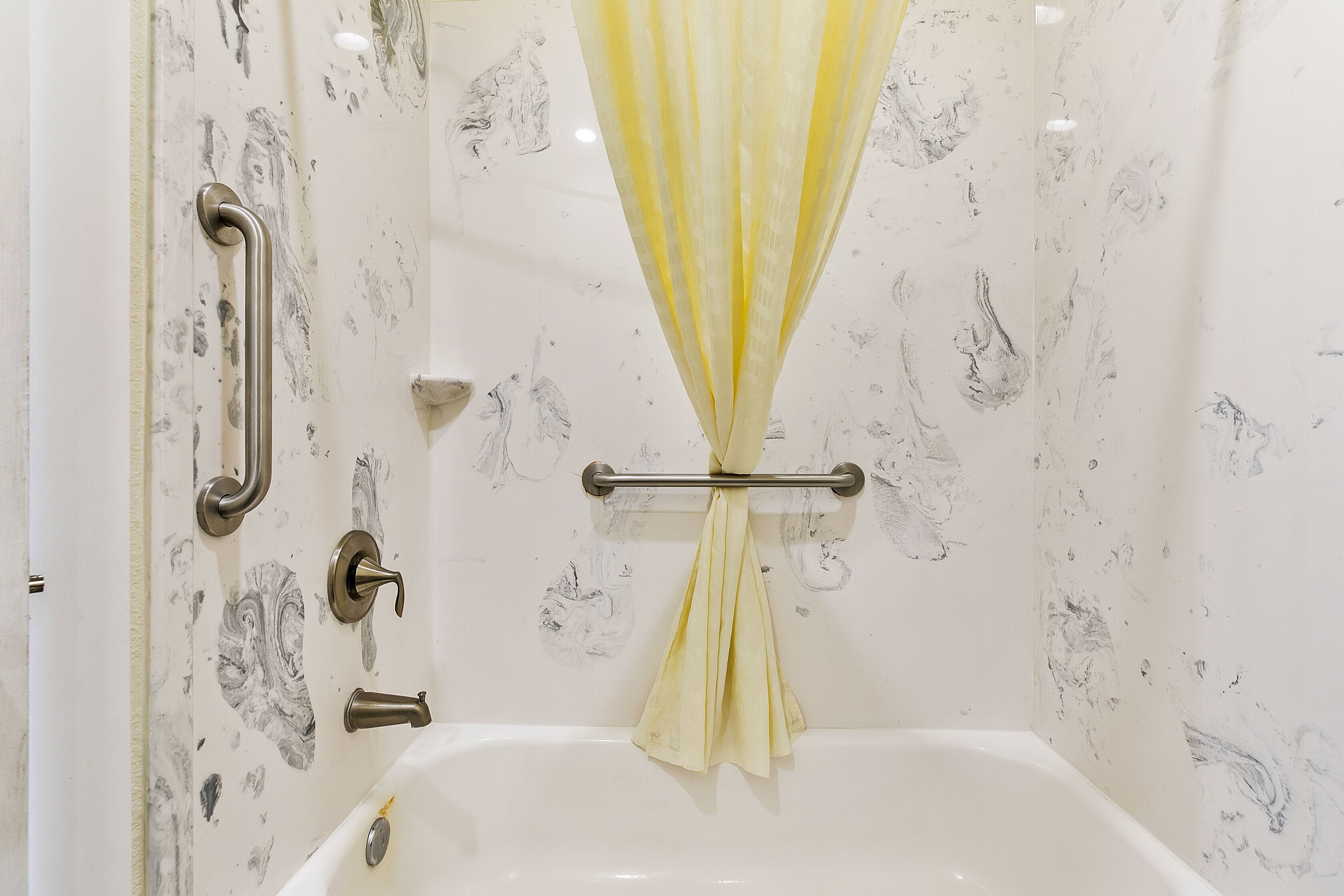 Une salle de bain équipée d’une baignoire, de barres d’appui et d’un rideau de douche.