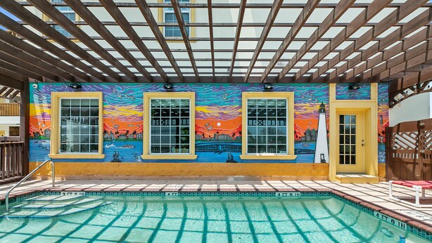 A pool area with a colorful mural, wooden pergola, and clear pool water. - Lighthouse Inn (South Padre Island)